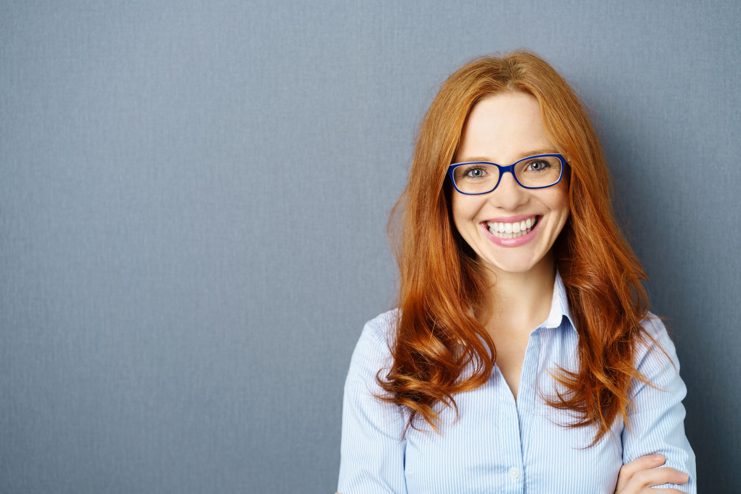 Portrait,Of,Young,Red-haired,Woman,Wearing,Glasses,Against,Blue,Background